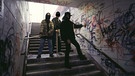 Mitglieder einer Jugendbande mit einer Eisenstange und einer Holzlatte stehen in einem Tunnel, ein Jugendlicher besprüht die Wand mit Graffitis. | Bild: picture-alliance / Rolf Kremming | Rolf Kremming