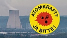 Aufkleber mit einem erstaunten Gesicht auf einer stilisierten Sonne und der Aufschrift "Atomkraft - Ja bitte!" neben einem AKW | Bild: picture-alliance/dpa, Montage: BR
