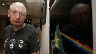 Graphic designer Storm Thorgerson stands next to his album cover of the Pink Floyd album 'The Dark Side of the Moon' during the opening of his exhibition 'Mind Over Matter: The Images of Pink Floyd' | Bild: picture alliance / ASSOCIATED PRESS | Yui Mok