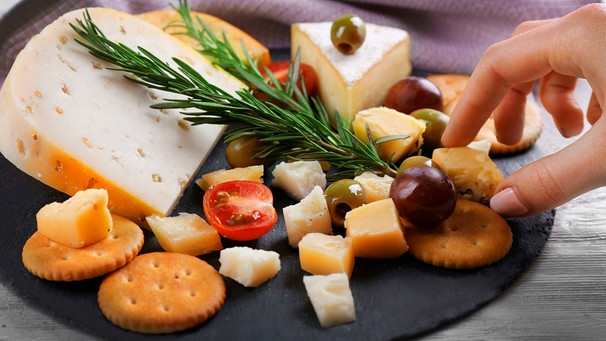 Eine Hand nimmt sich ein Stück Käse von einer Käseplatte | Bild: mauritius bilder / pixel-shot / alamy / Alamy Stock Fotos